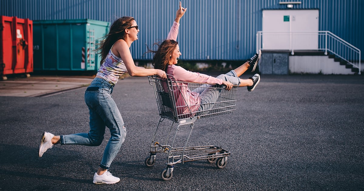 a woman pushing a shopping cart with her friend inside it